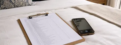 Prancheta com checklist impresso de vistoria ao lado de um celular, ambos apoiados sobre a cama de um quarto