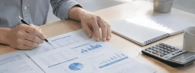 Pessoa revisando relatório financeiro impresso com gráficos, caneta na mão e calculadora ao lado