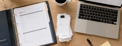 Pasta com documentos, recibos organizados e notebook aberto com planilha sobre mesa de escritório, vista de cima