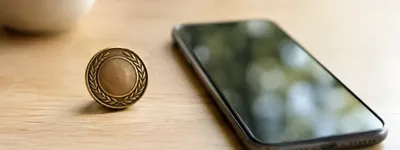 Medalha dourada com coroa de louros ao lado de um celular com a tela escura, sobre uma mesa de madeira clara