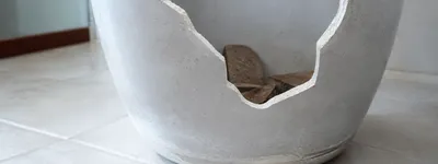 Vaso de cimento grande com uma quebra grande na borda, mostrando um dano físico dentro do imóvel