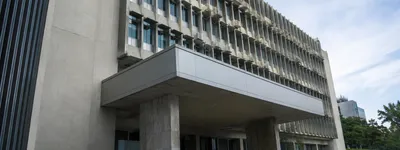 Fachada de prédio público em concreto aparente, estilo institucional, com entrada coberta e escadaria de acesso