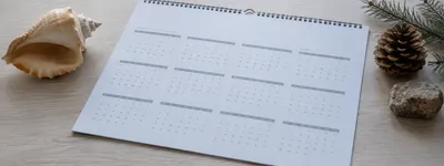 Calendário anual sobre a mesa, com uma concha do mar de um lado e uma pinha com galho de pinheiro e pedra do outro, representando as duas estações opostas