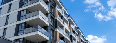 Fachada de um prédio residencial moderno com vários andares de sacadas envidraçadas, visto de baixo contra o céu azul